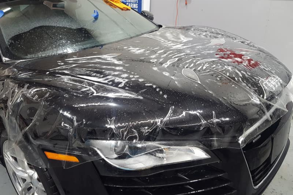 . A car wrapped in plastic, showcasing a sleek black paint job, stands out in a unique protective covering.