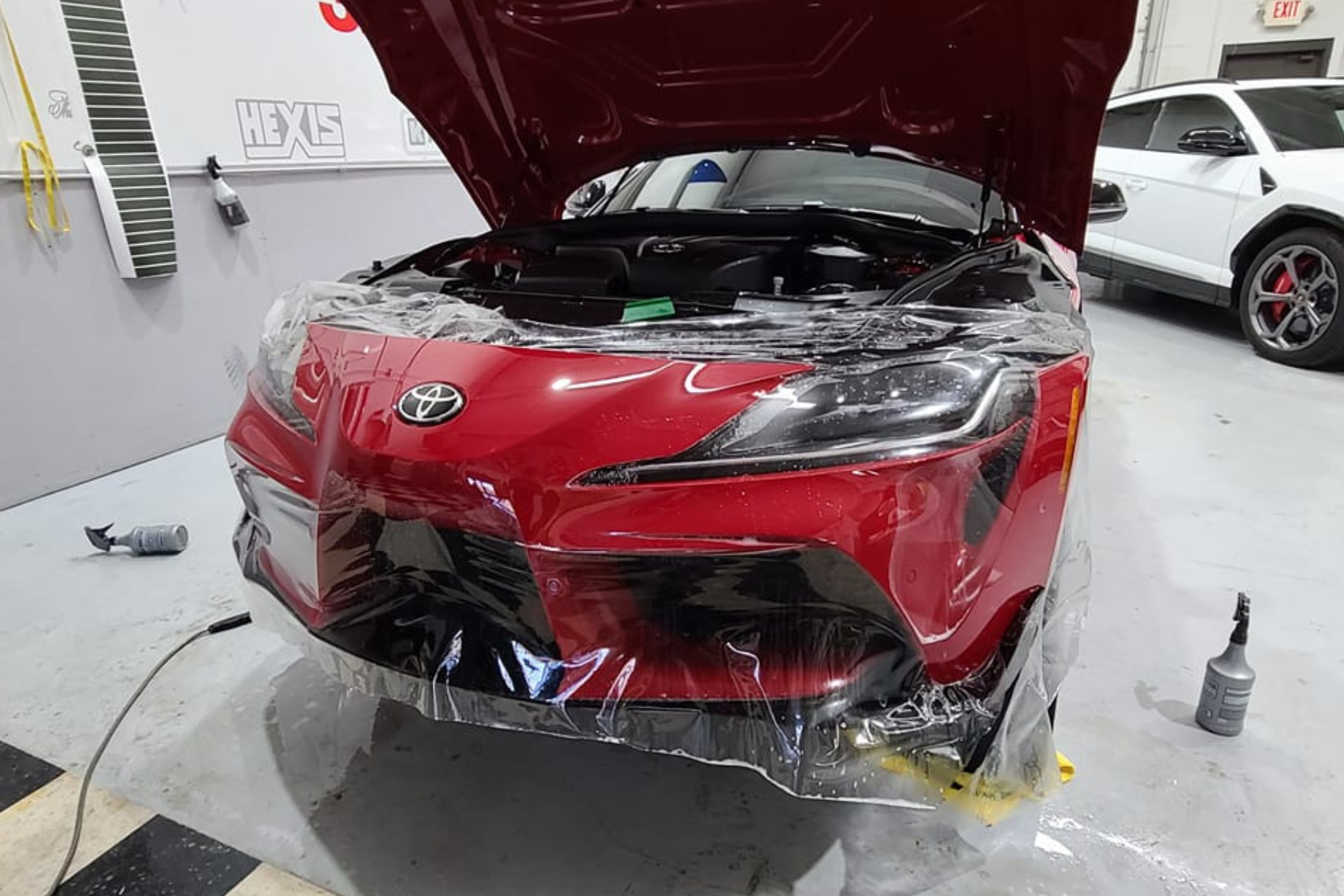 Inside a garage, a red sports car is in the process of being painted, highlighting the attention to detail in the work.